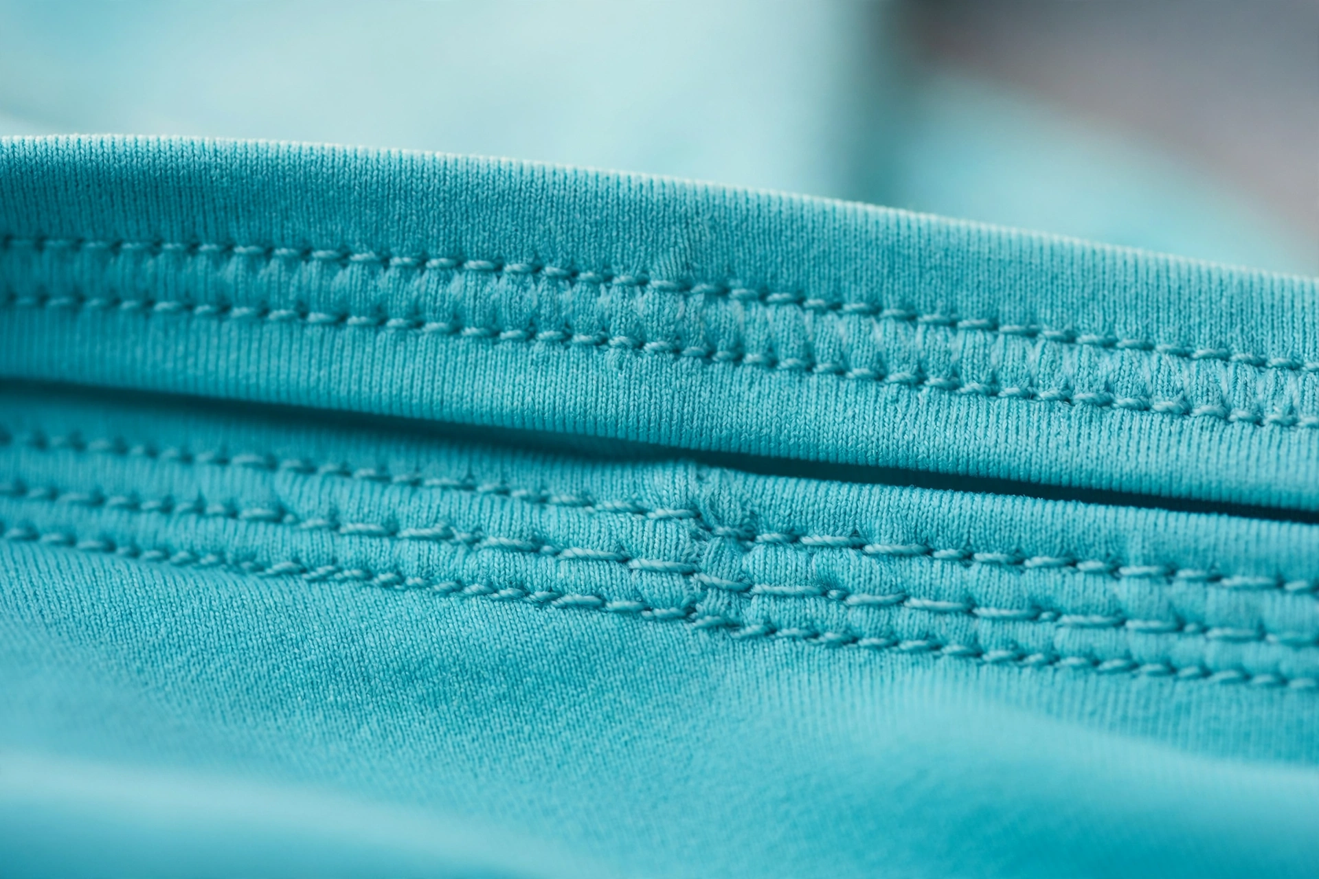 Close-up of neat parallel stitching rows on turquoise stretch swim fabric