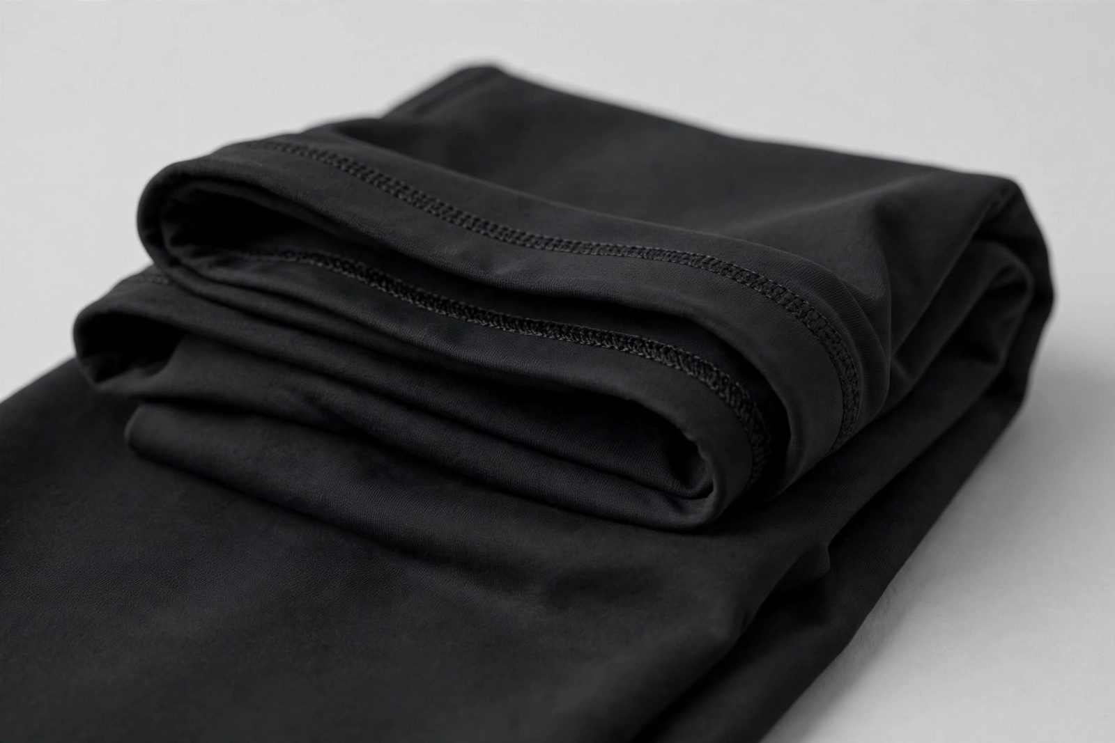 Close-up of a folded black athletic leggings waistband with neat coverstitch seams on a plain background (concept illustration)